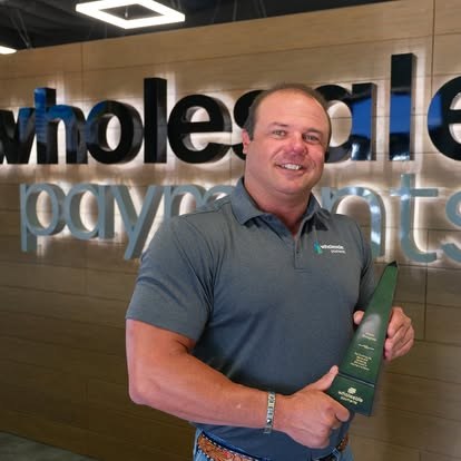 Rep holding an award in front of the Wholesale Payments sign